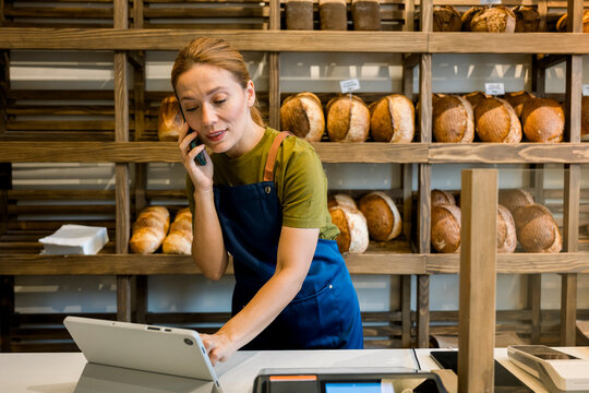 Bakery owner smiling while taking order on mobile and using tablet