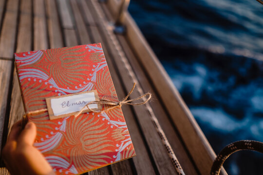 Hand holding a decorated gift box on a sailboat deck at sea