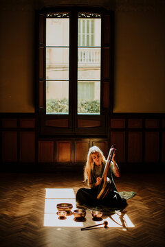 Musician playing lyre and singing bowls indoors in sunlight