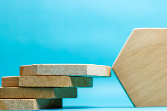 A close-up shot of stacked wooden hexagonal pieces forming a staircase next to an upright block against a solid blue backdrop. High Quality Photo