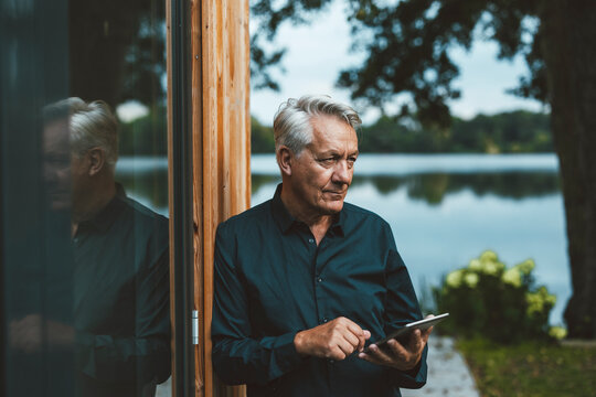 Senior man with tablet PC standing by glass wall at backyard