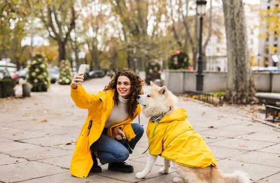 Happy young woman taking selfie with dog through smart phone at footpath