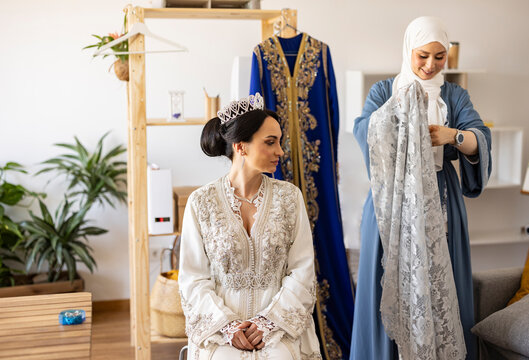 Smiling bride with wedding designer holding veil