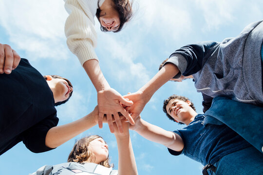 Five friends stacking their hands looking at each other, seen from below
