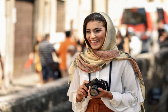 Spain, Granada, young Arab tourist woman wearing hijab, using camera during sightseeing in the city