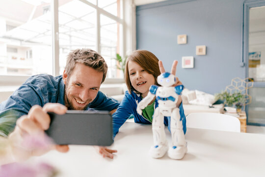 Happy father and son taking a selfie with robot on table at home