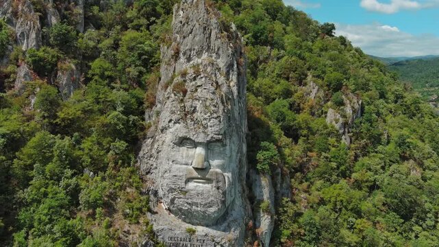 Aerial around view of stone carved statue portrait of ancient dacian king Decebal. Sculpture located on shore of Danube River, Romania, 4k