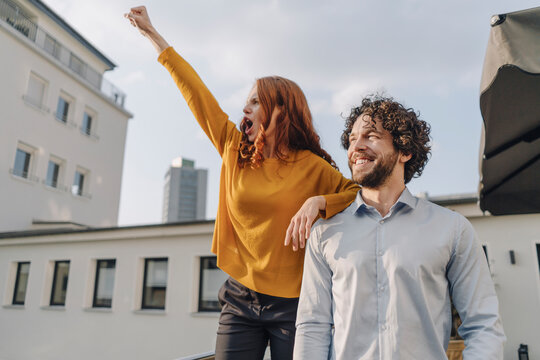 Woman with colleague on roof terrace clenching fist
