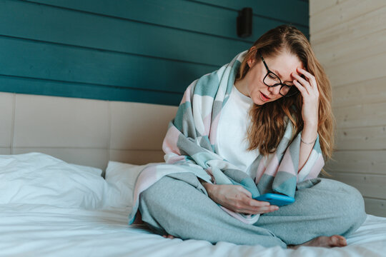 Disappointed woman using smart phone in bedroom at home