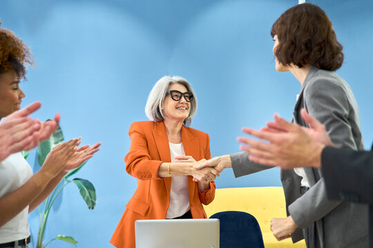 Coworkers clap to celebrate successful handshake in the office