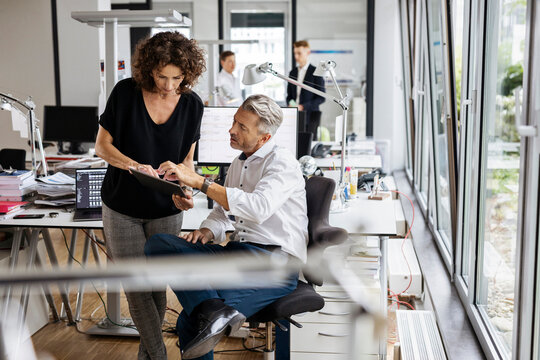Business people using digital tablet while working with colleagues in background at open plan office
