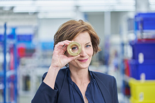 Confident female manager looking through brass object in factory