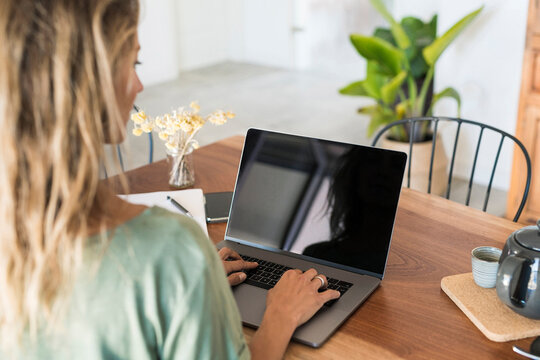 Close-up of woman using laptop on wooden table at home