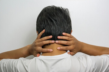 Fototapeta premium Person in white shirt holding neck with both hands, highlighted pain area, medical advertising concept for neck strain treatment.