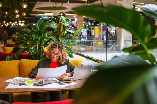 Architect reading blueprint at table in biophilic workspace