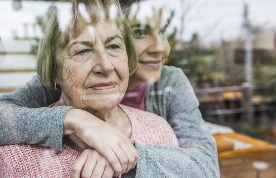Caregiver hugging senior woman at window
