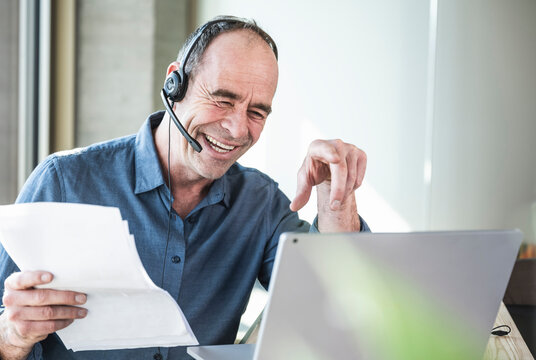 Happy businessman wearing headset holding document sitting in office