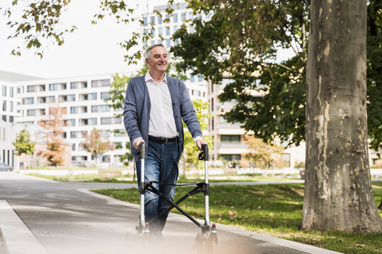Smiling senior man walking with mobility walker on footpath