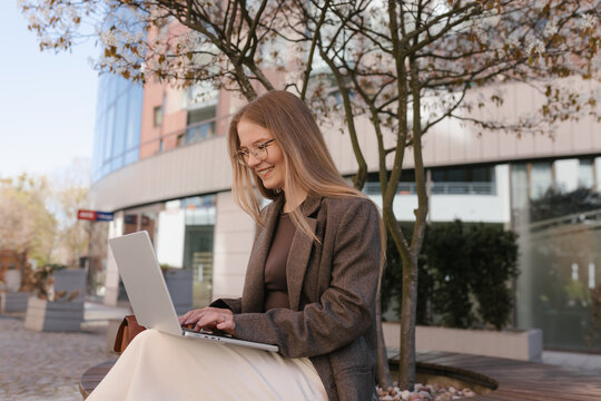 Smiling businesswoman working on laptop outdoors in the city
