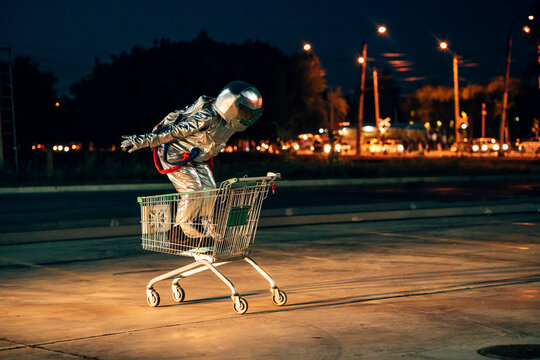Spaceman in the city at night on parking lot inside shopping cart