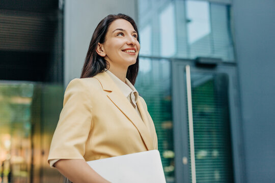 Smiling businesswoman holding a laptop outdoors in the city