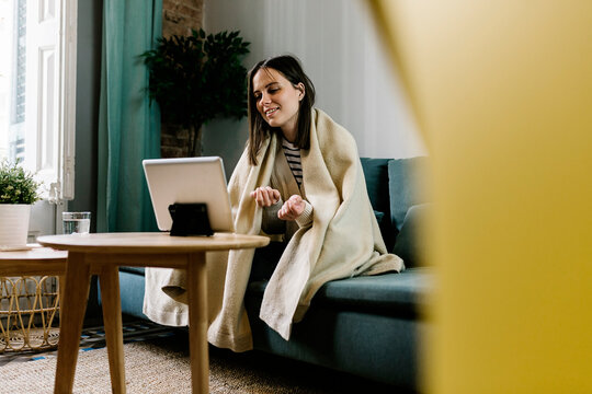 Woman wrapped in blanket talking during video call through digital tablet at home