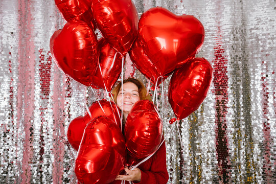 Happy woman holding heart shaped balloons in front of sequin curtain