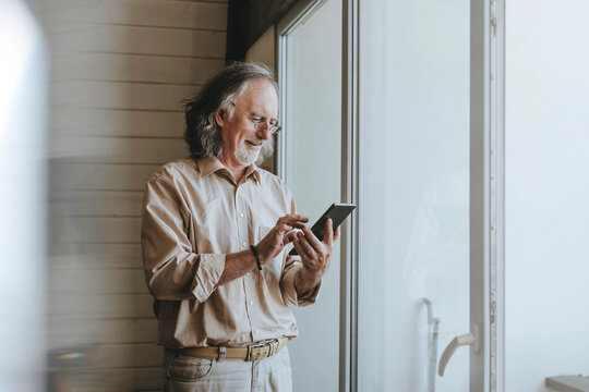 Smiling senior man standing near window using tablet PC at home