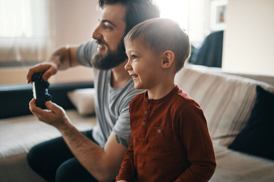 Happy little boy playing computer game with his father at home