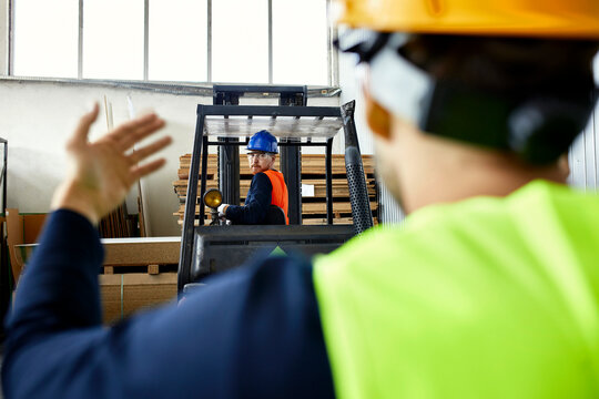 Worker assisting man on forklift in factory