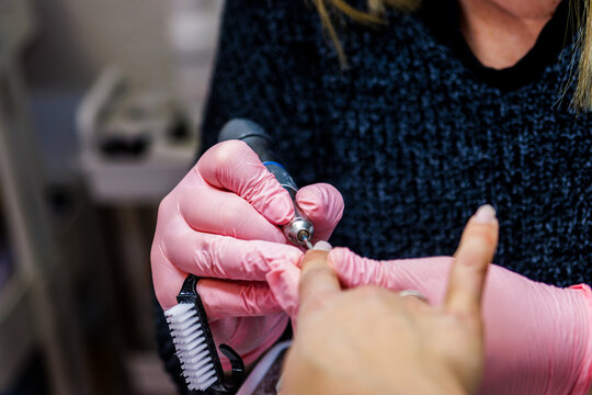 Manicurist working on client nail using drill tool in beauty salon for professional treatment