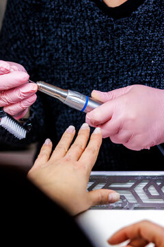 Manicurist working on client nails using an electric file in a beauty salon