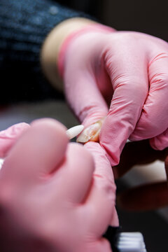 Professional manicurist with pink gloves performing nail care using an electric file