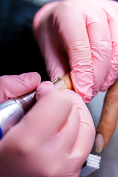 Manicurist working on client's cuticle using an electric nail file tool for professional nail care