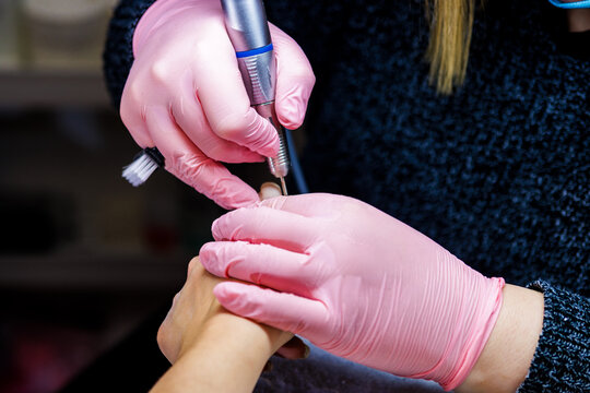 Manicurist wearing pink gloves using a nail drill tool on a client for a cosmetic spa procedure