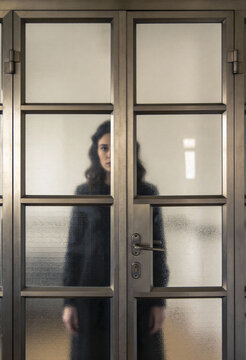 Junge Frau steht hinter einer verschlossenen Glast&uuml;r &ndash; Konzept f&uuml;r Isolation, Barrieren, Depression und Ausgrenzung