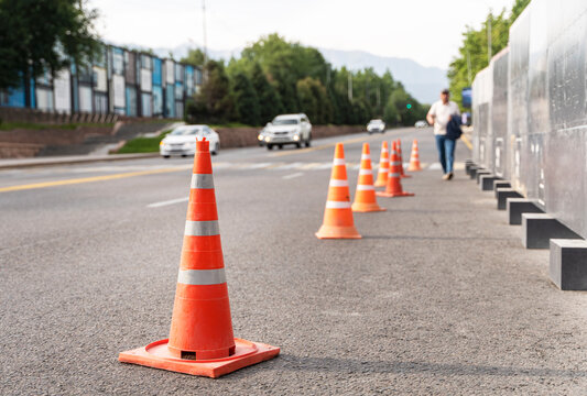 Orange traffic cones marking roadside safety zone on urban street with moving vehicles and pedestrian
