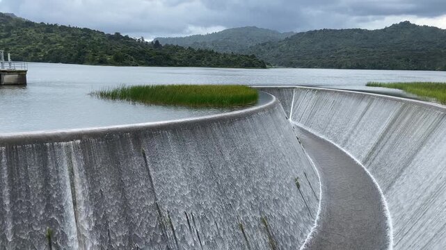 Curved spillway overflow at reservoir surrounded by native forest in New Zealand