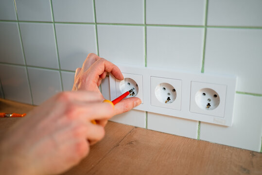 Hand installing electrical outlet socket on kitchen wall, using a screwdriver for home renovation, electrical work, and power supply connection during apartment repair