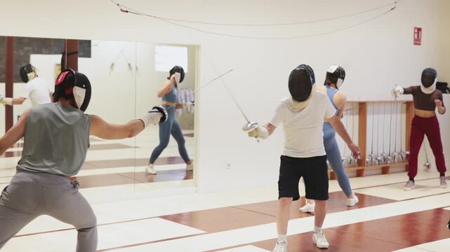 Women in protective equipment conduct a training fencing match. Two athletes are fighting on a fencing track in a modern sports center 