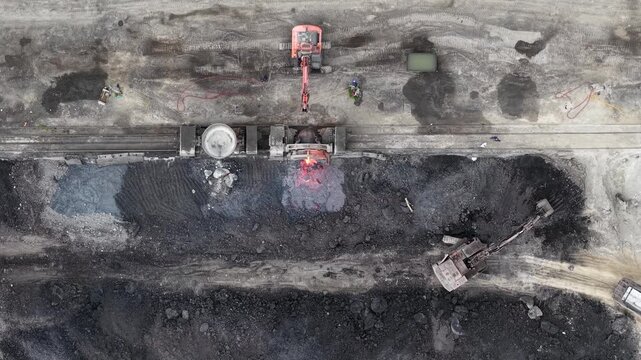 An aerial top view perspective shows heavy excavators handling molten slag and debris at an industrial steel factory in Hungary.