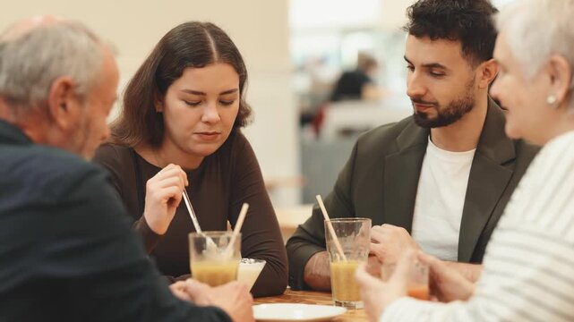 Large friendly family gathered at table to have meeting in restaurant or cafe. Relatives drink juice or coffee, and socialize. People participate in discussion during meeting