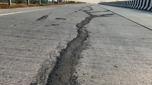 POV tracking shot moving along a long crack in a concrete highway surface, revealing damaged pavement, broken edges, and road deterioration from the perspective of a moving vehicle under daylight cond
