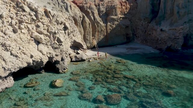 A couple of men and women walk at the Tsigrado BeachMilos, Greece, where crystal-clear waters gently lap against striking rock formations. Enjoy tranquil moments in this hidden paradise
