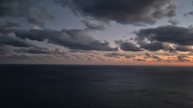 Sunset Ocean Clouds roll dramatically over the dark seascape and rugged coastal cliffs after the fiery sundown