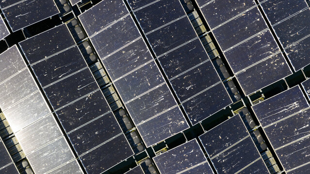 Aerial view of rows of solar panels on a floating solar farm with visible dirt and sun reflections on the dark surfaces in Zwolle, Overijssel, Netherlands.
