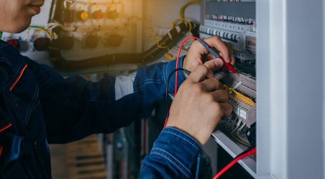Electrician builder engineer testing and screwing equipment in fuse box and repairing of modern electricity power station using voltmeter. Automatic control cabinet