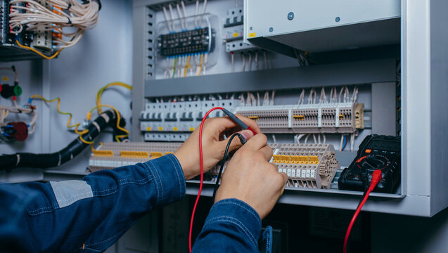 Electrician builder engineer testing and screwing equipment in fuse box and repairing of modern electricity power station using voltmeter. Automatic control cabinet