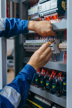 Electrician builder engineer testing and screwing equipment in fuse box and repairing of modern electricity power station using voltmeter. Automatic control cabinet