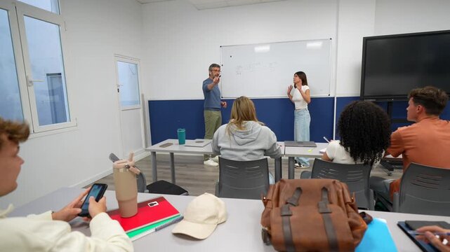 Female student standing at the whiteboard next to her male professor, explaining a concept to her classmates during a university lecture, with some students taking notes while others are distracted